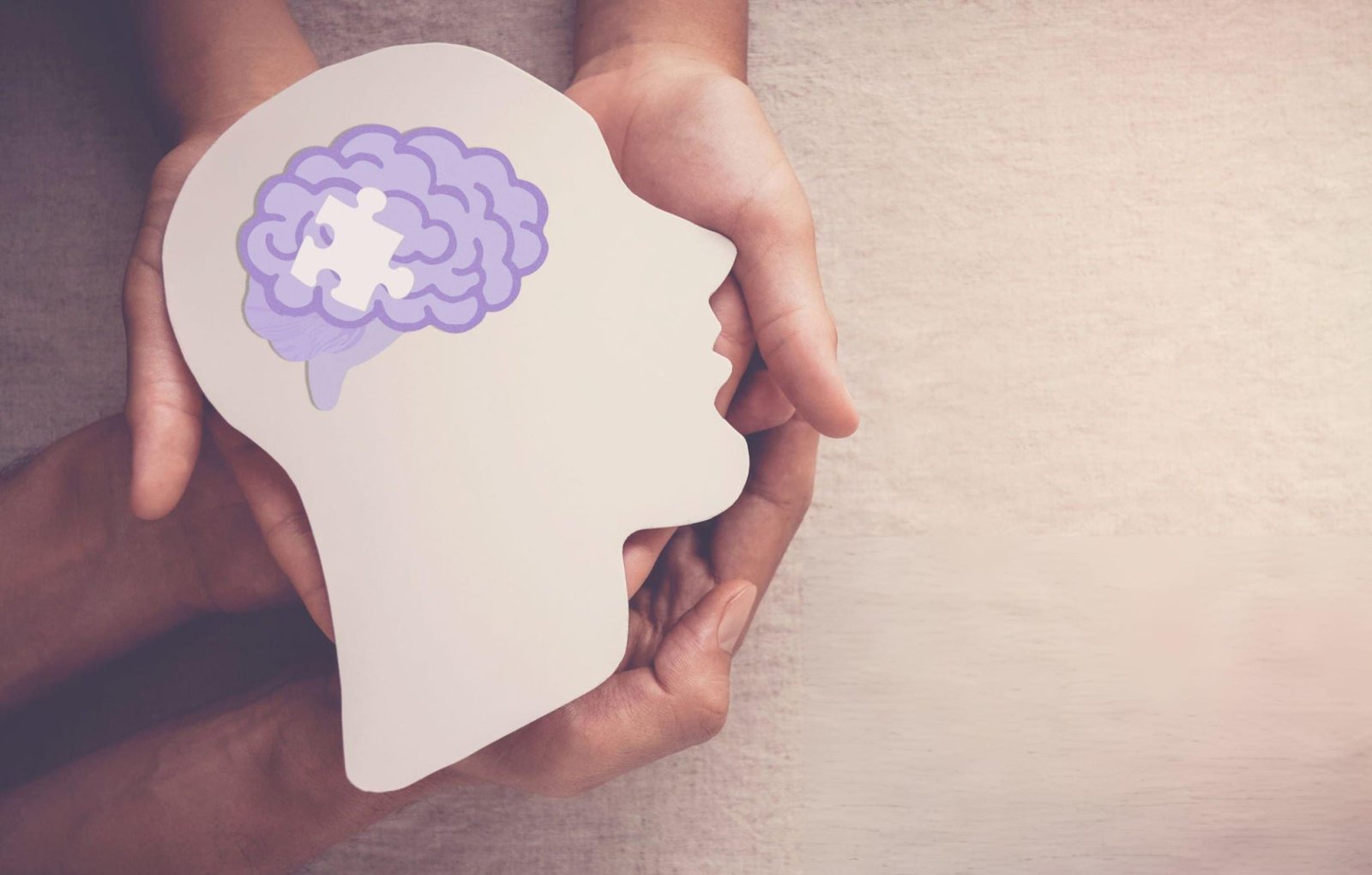 "A pair of hands holding a cutout of a human head in profile, with an illustration of a brain inside that has a puzzle piece missing. This visual metaphor represents mental health and the process of healing and understanding the mind, relevant to heal from trauma with DBT.